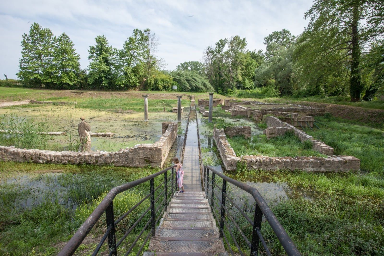 A boardwalk crosses water-surrounded stone ruins and columns at the ancient sanctuary of Dion near Mount Olympus.